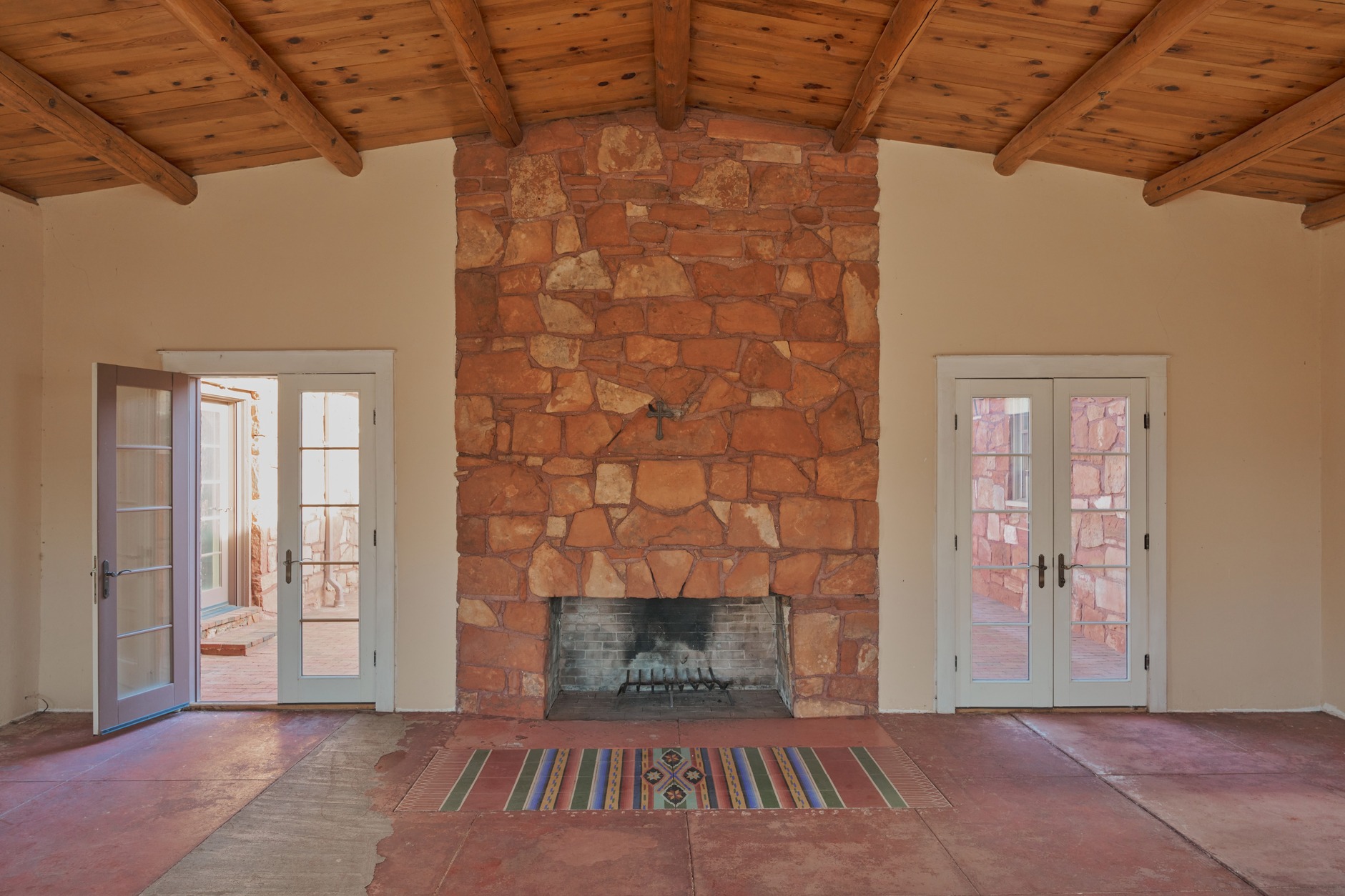 Great room with massive stone fireplace, timber ceiling, and hand-painted tile rug